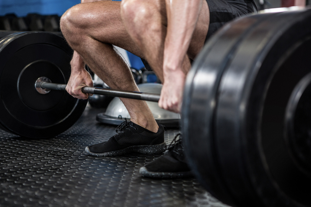 Low section of man lifting barbell in fitness studio